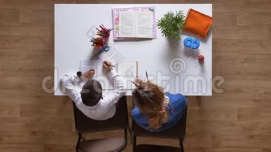 年轻的母亲帮助儿子做作业，坐在桌子后面，孩子做作业，顶着木地板打拍子